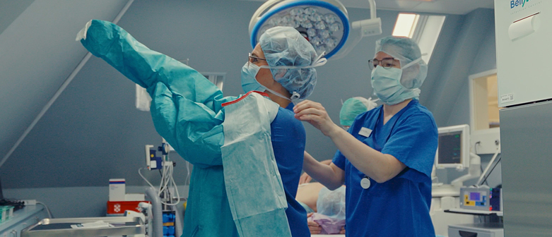 Zwei Mitarbeitende des OP-Teams der Venenklinik Bellevue helfen sich gegenseitig beim Anlegen der OP-Kleidung.
